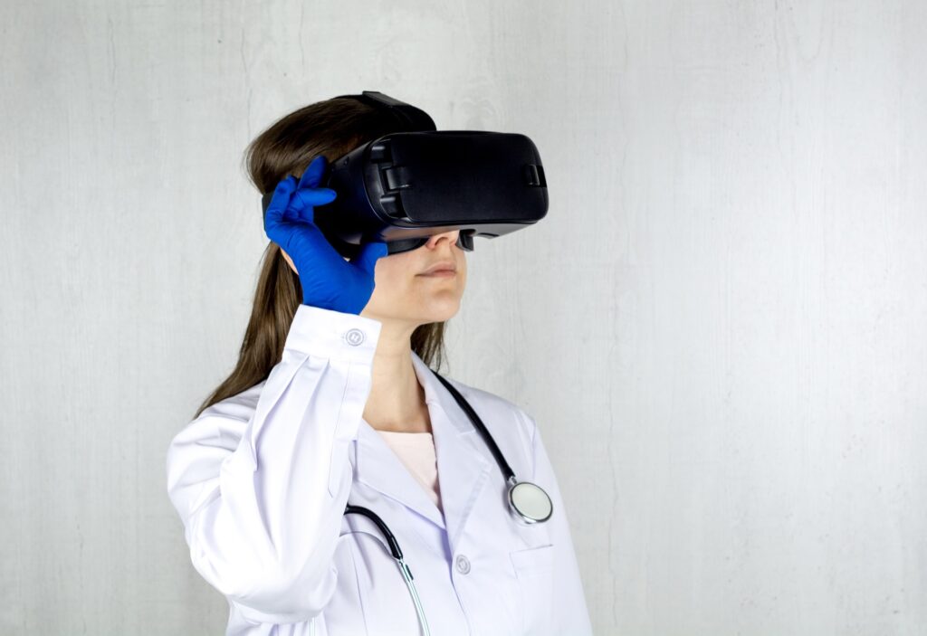 Valkotakkinen, pitkähiuksinen naislääkäri pitää mustia VR-laseja kasvoillaan ja katsoo niiden läpi. Kaulassa hänellä roikkuu stetoskooppi. 